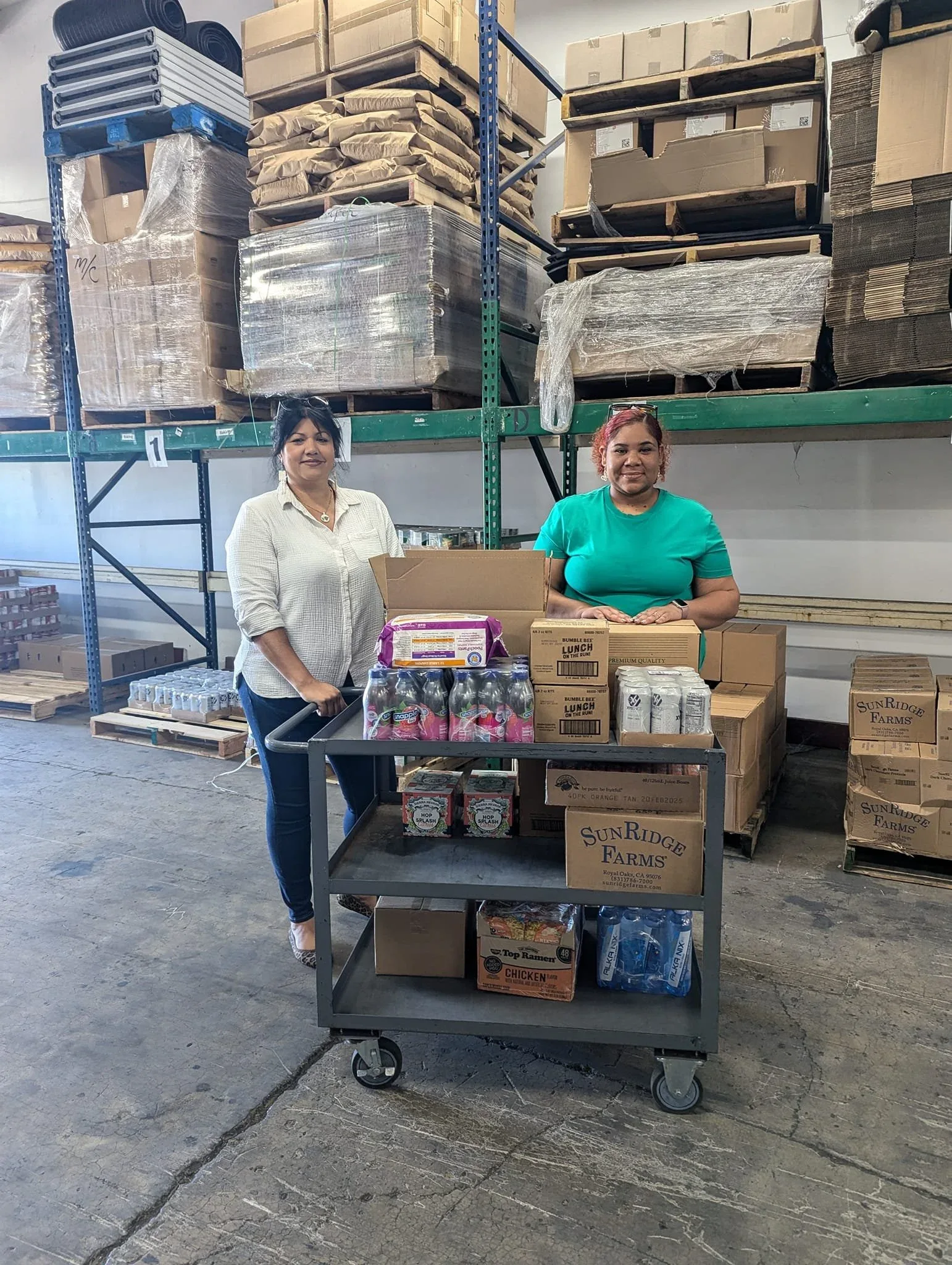 Two people with a cart of supplies in a warehouse.