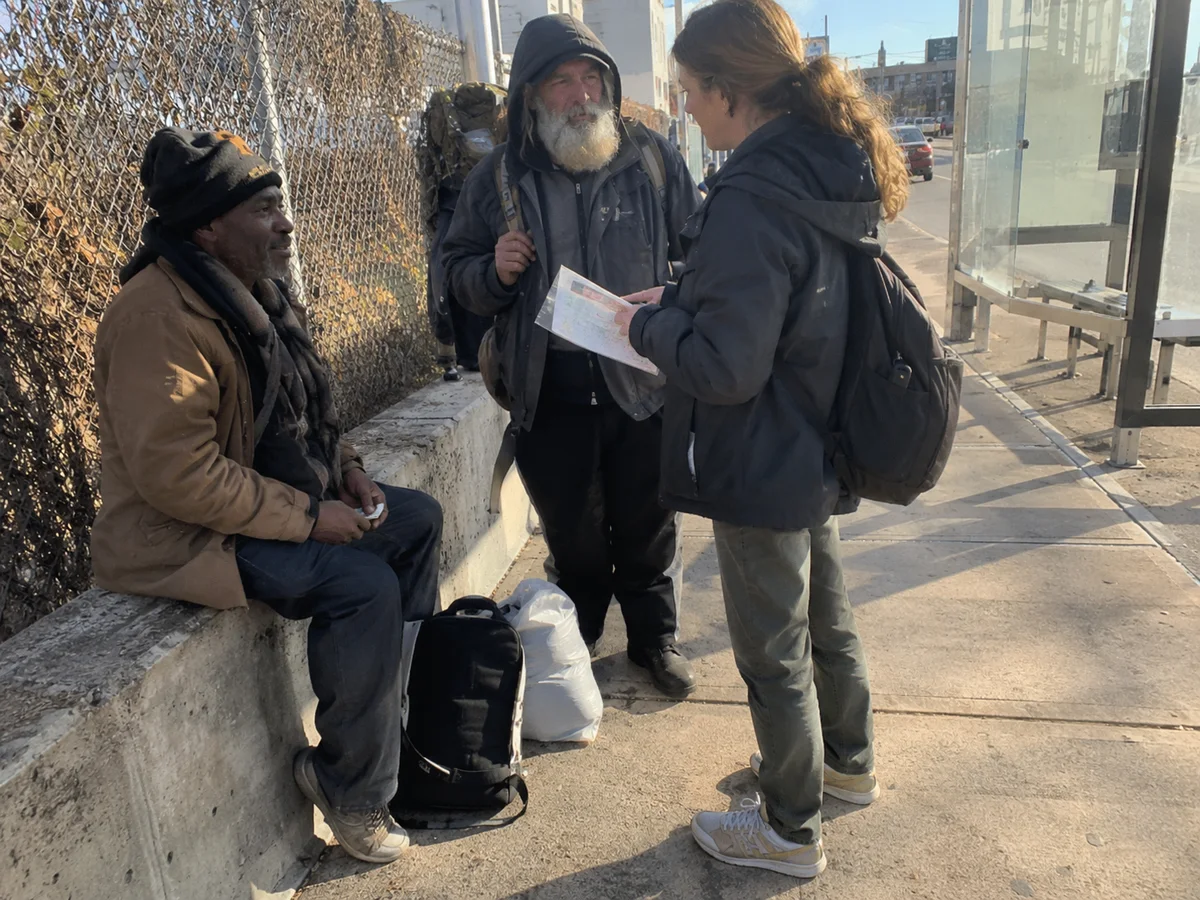 An outreach worker speaking with two people near a bus shelter.