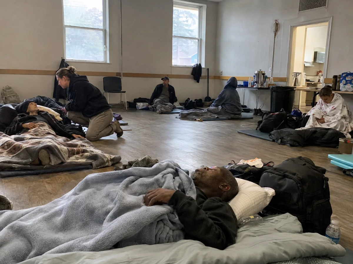 Guests resting on mats inside an overnight shelter.